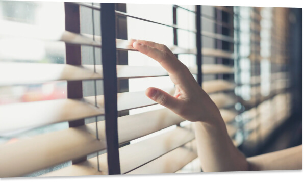 Close up on a hand on some wood blinds as if a person were looking out the window