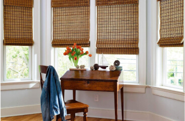 Natural Woven shades partially covering bay windows near a writing desk