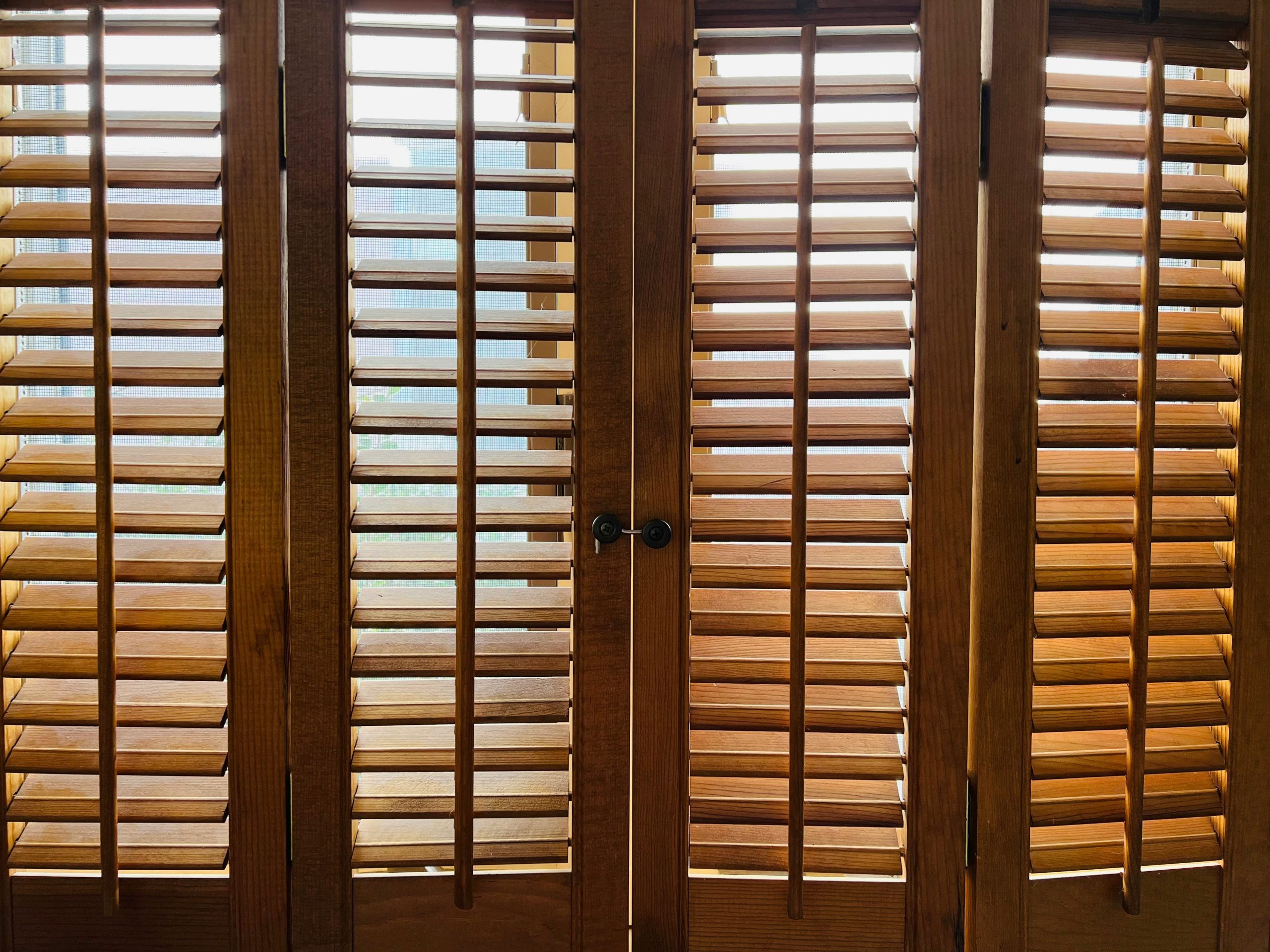 Brown wooden blinds shade a big window from the outside light